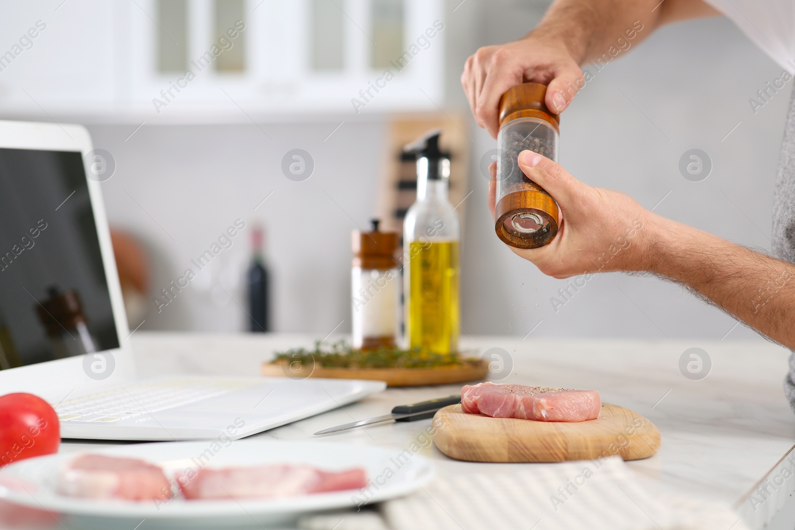 Photo of Man making dinner while watching online cooking course via laptop in kitchen, closeup