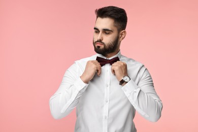 Portrait of handsome man adjusting bow tie on pink background