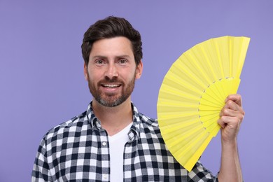 Photo of Happy man holding hand fan on purple background