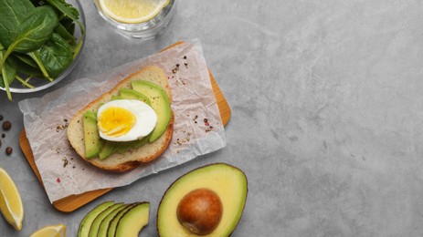 Photo of Delicious sandwich with boiled egg, pieces of avocado and basil leaves on gray table, flat lay. Space for text