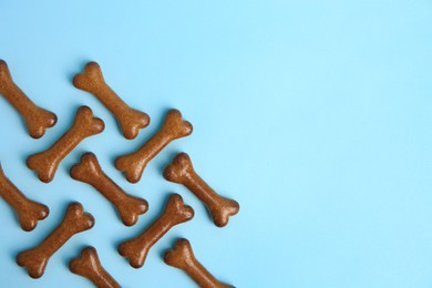 Photo of Bone shaped dog cookies on light blue background, flat lay. Space for text