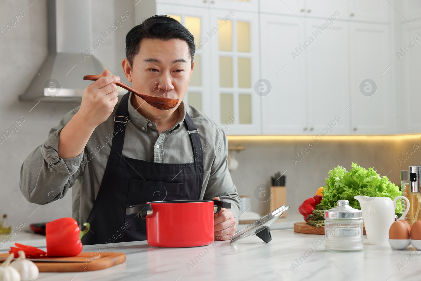 Photo of Cooking process. Man tasting dish at countertop in kitchen