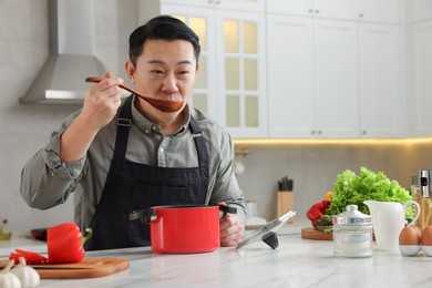 Photo of Cooking process. Man tasting dish at countertop in kitchen