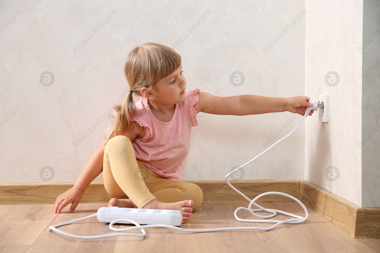 Photo of Little child playing with electrical socket and power strip plug at home. Dangerous situation