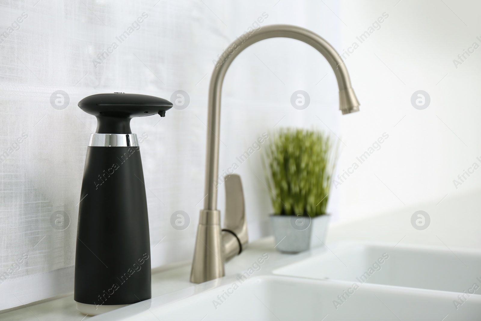 Photo of Modern automatic soap dispenser near sink in kitchen