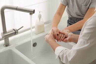 Mother and daughter washing hands with liquid soap together at home, closeup