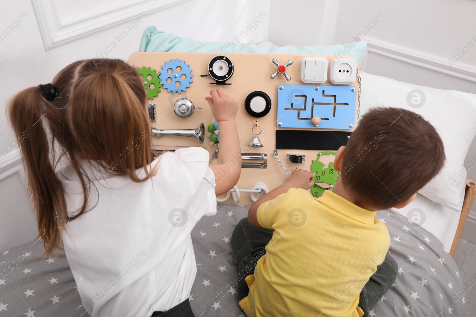 Photo of Little boy and girl playing with busy board on bed in room