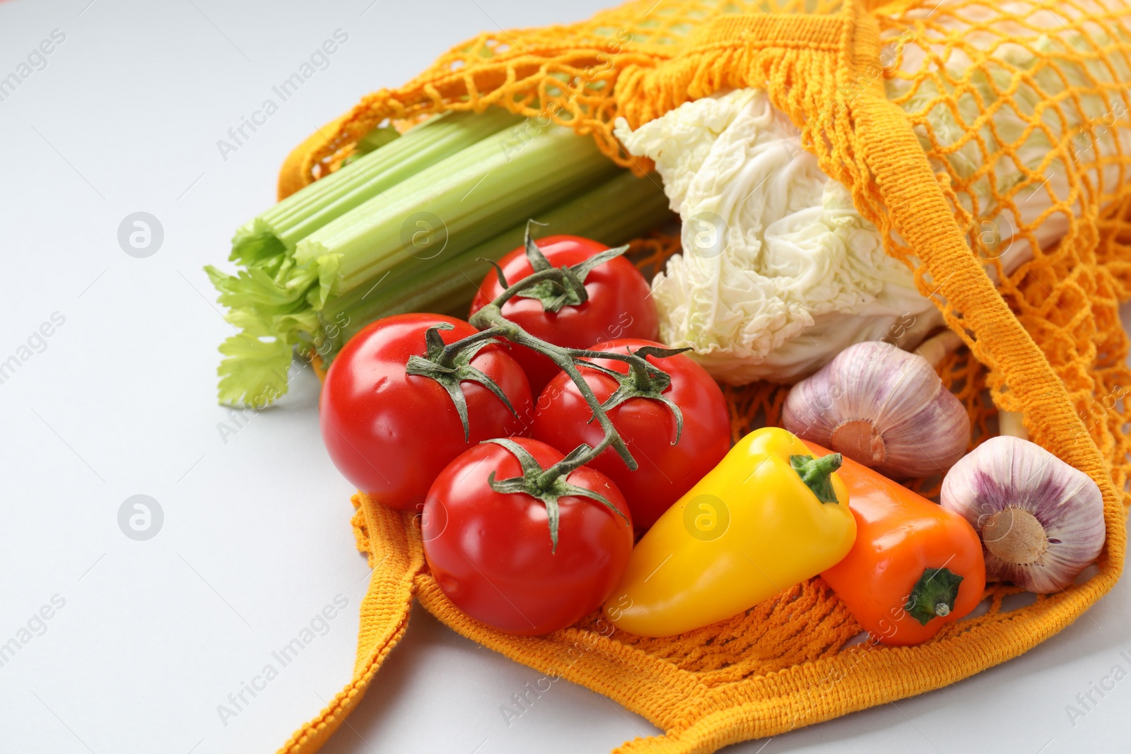Photo of String bag with different vegetables on light grey background, closeup