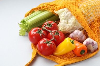 Photo of String bag with different vegetables on light grey background, closeup