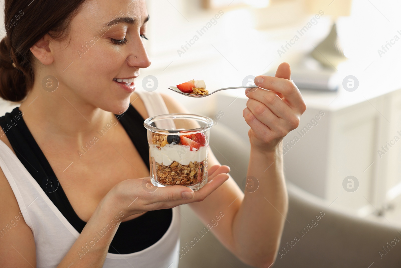 Photo of Woman eating tasty granola with fresh berries and yogurt at home, closeup