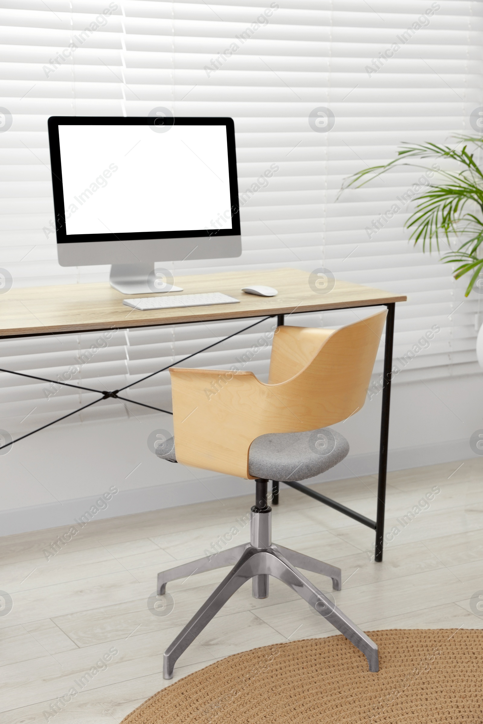 Photo of Stylish office interior with comfortable chair, desk, computer and houseplant