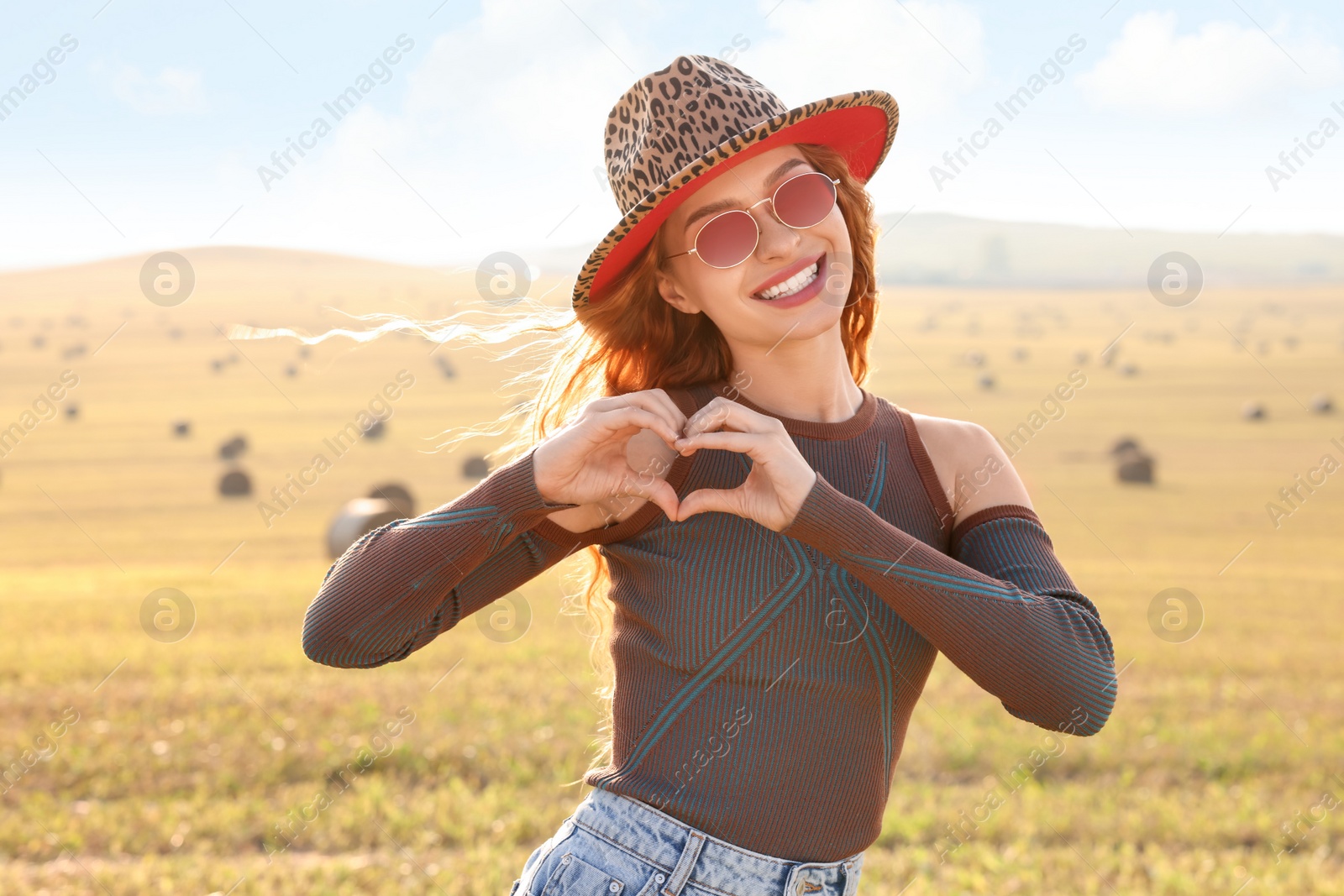 Photo of Beautiful happy hippie woman making heart with hands in field