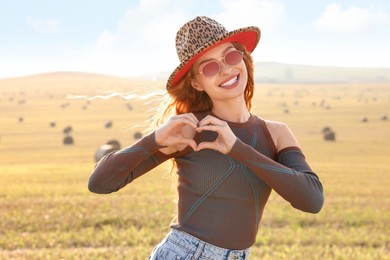 Beautiful happy hippie woman making heart with hands in field