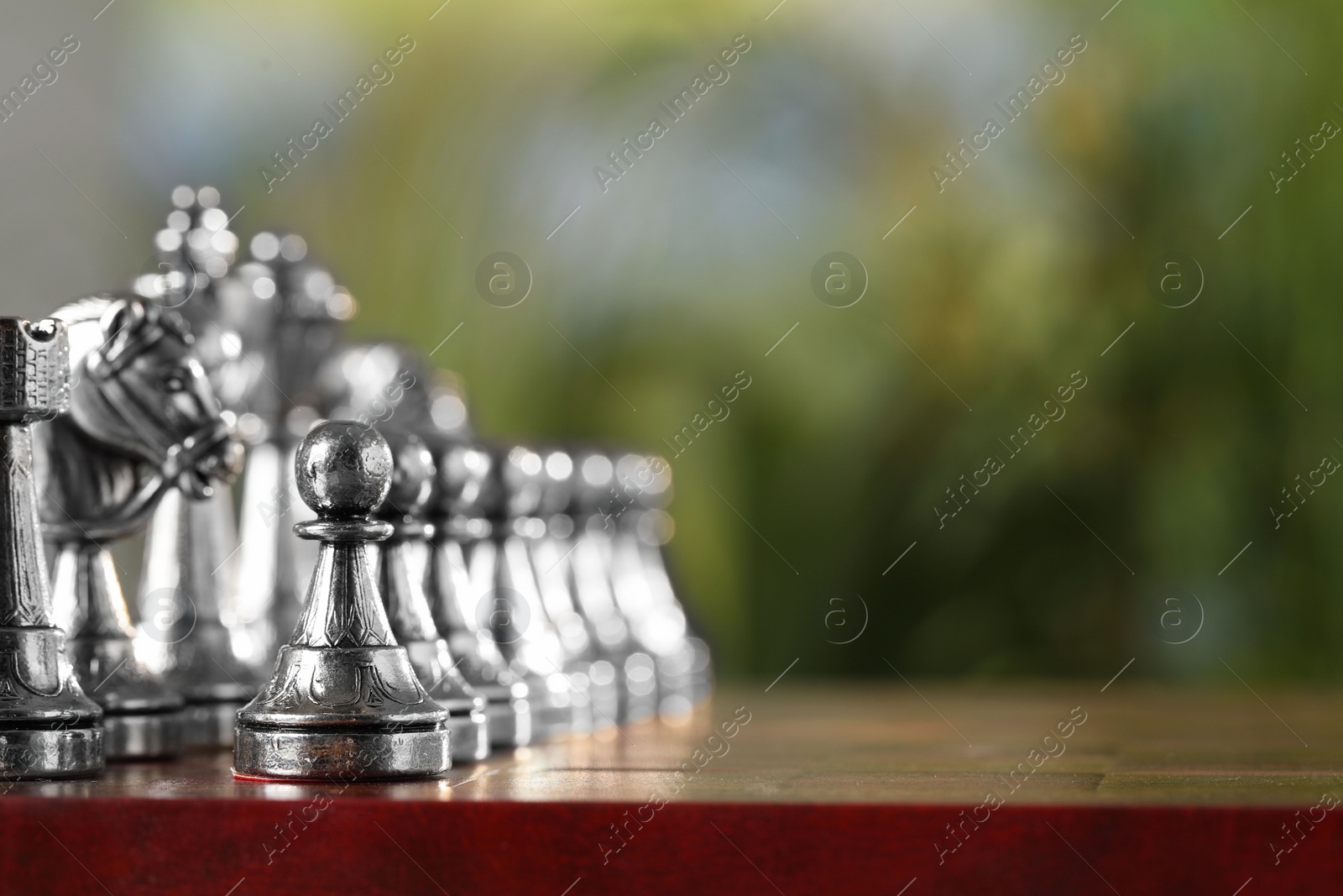Photo of Silver chess pieces on game board against blurred background, space for text