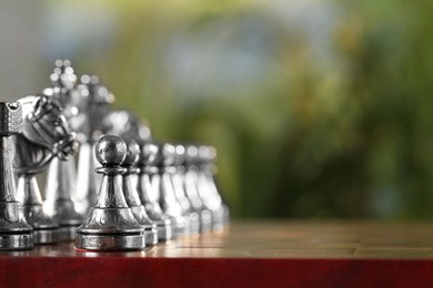 Photo of Silver chess pieces on game board against blurred background, space for text
