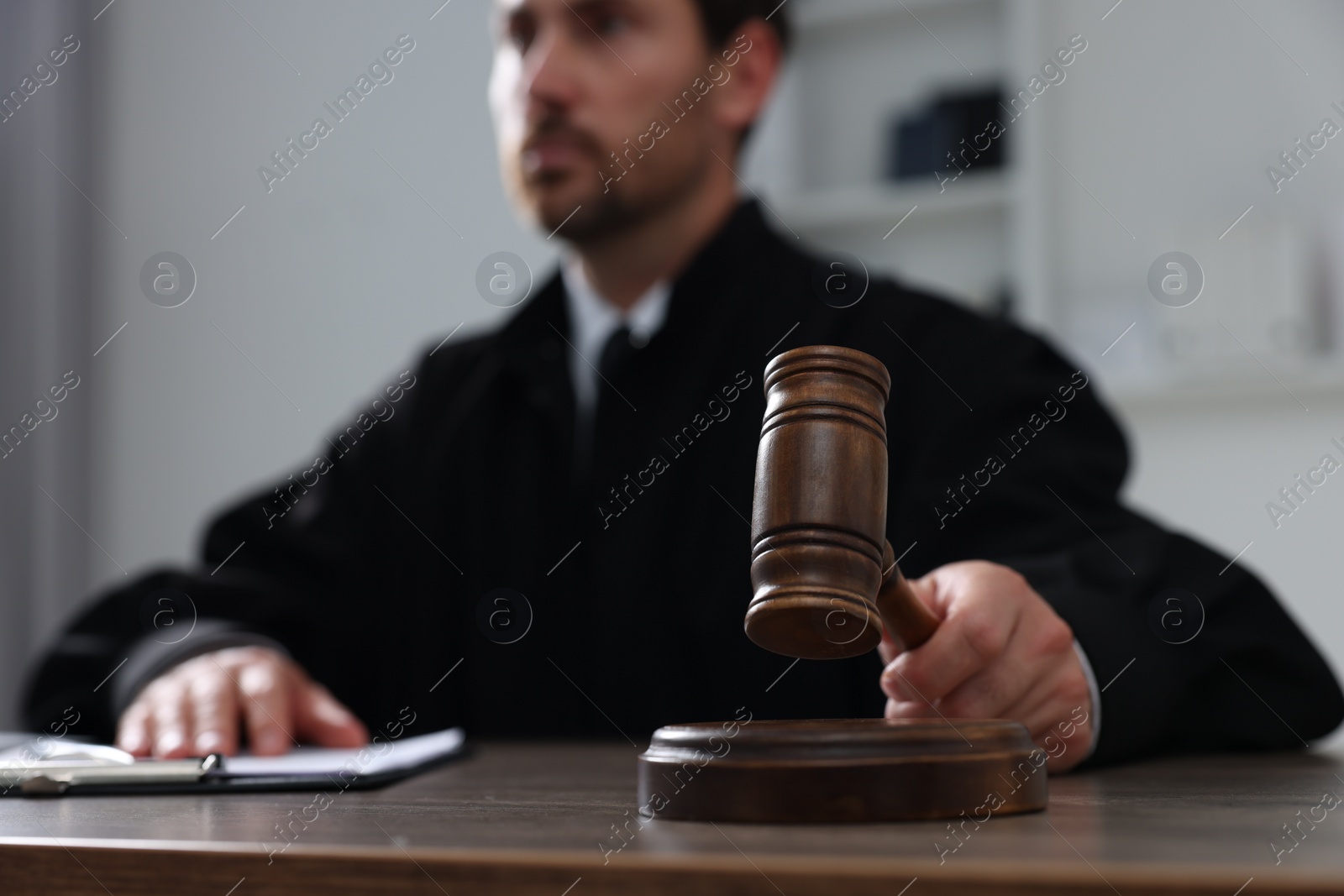 Photo of Judge with gavel and papers sitting at wooden table indoors, selective focus