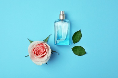 Bottle of perfume and rose on color background, top view