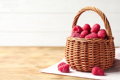 Wicker basket with delicious ripe raspberries on wooden table against light background, space for text