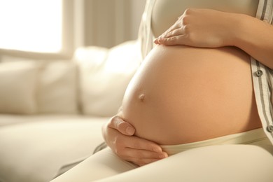 Pregnant woman touching her belly indoors, closeup