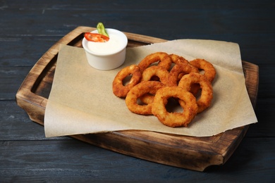 Photo of Wooden board with tasty onion rings and sauce on table