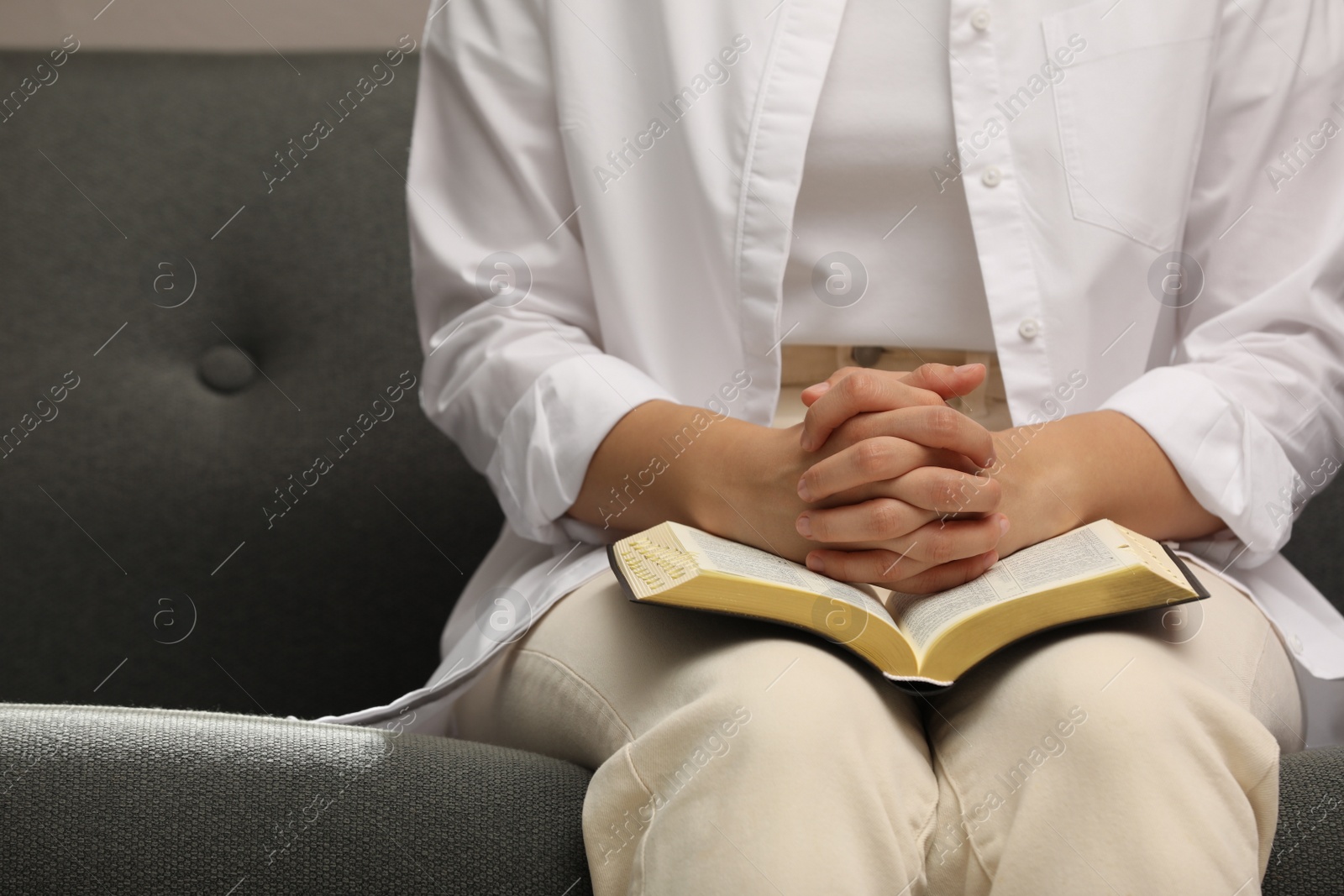 Photo of Religious woman praying over Bible indoors, closeup