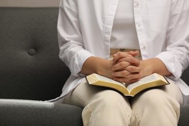 Photo of Religious woman praying over Bible indoors, closeup