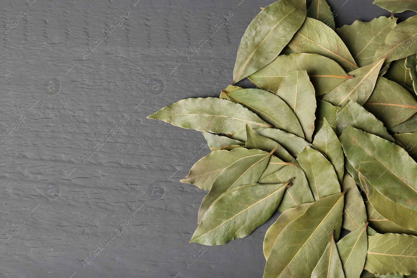 Photo of Pile of aromatic bay leaves on gray wooden table, top view. Space for text