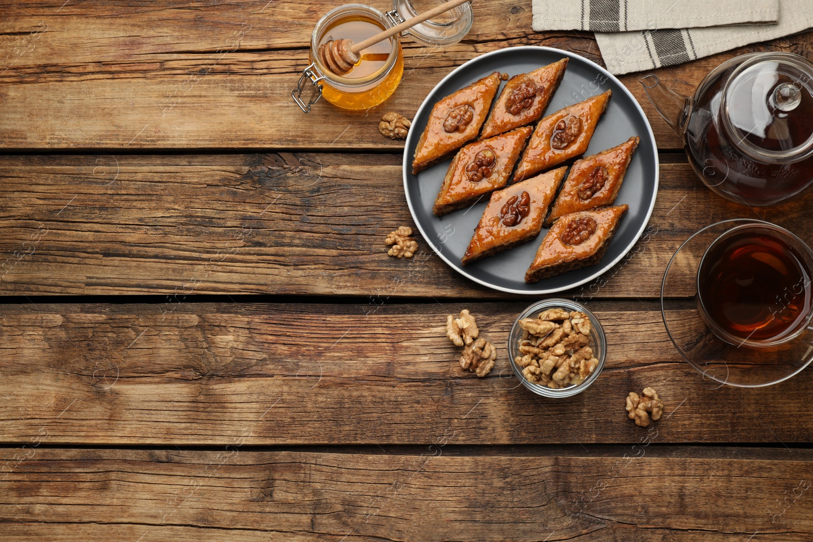 Photo of Delicious sweet baklava with walnuts, honey and hot tea on wooden table, flat lay. Space for text