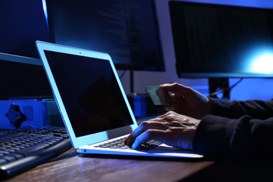 Photo of Hacker with computers and credit card in dark room, closeup. Cyber crime