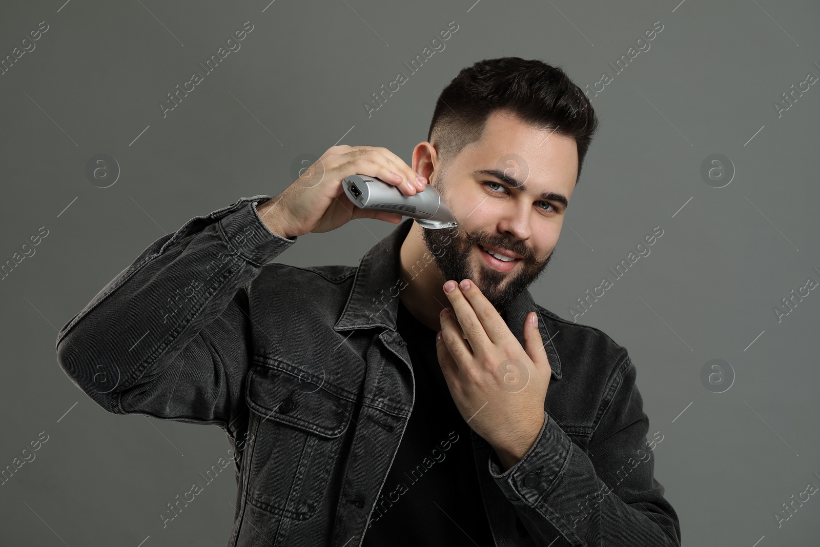 Photo of Handsome young man trimming beard on grey background