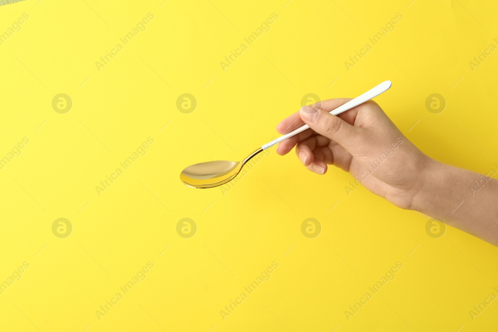 Photo of Woman holding empty table spoon on color background, closeup