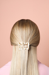 Photo of Young woman with beautiful gold hair clip pin on pink background, back view