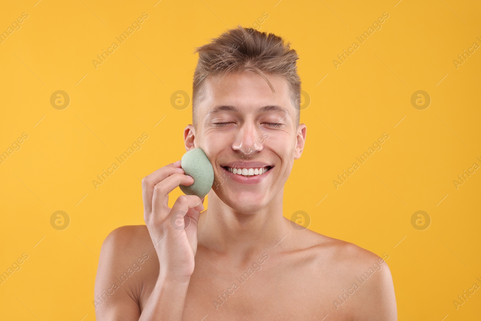 Photo of Happy young man washing his face with sponge on orange background