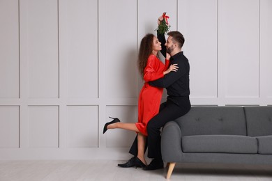 Photo of Lovely couple under mistletoe bunch near light grey wall indoors. Space for text
