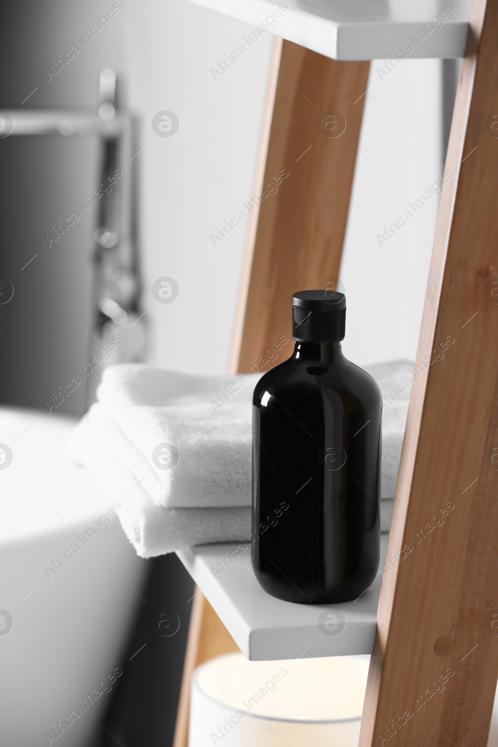 Photo of Bottle of bubble bath and towels on shelf in bathroom