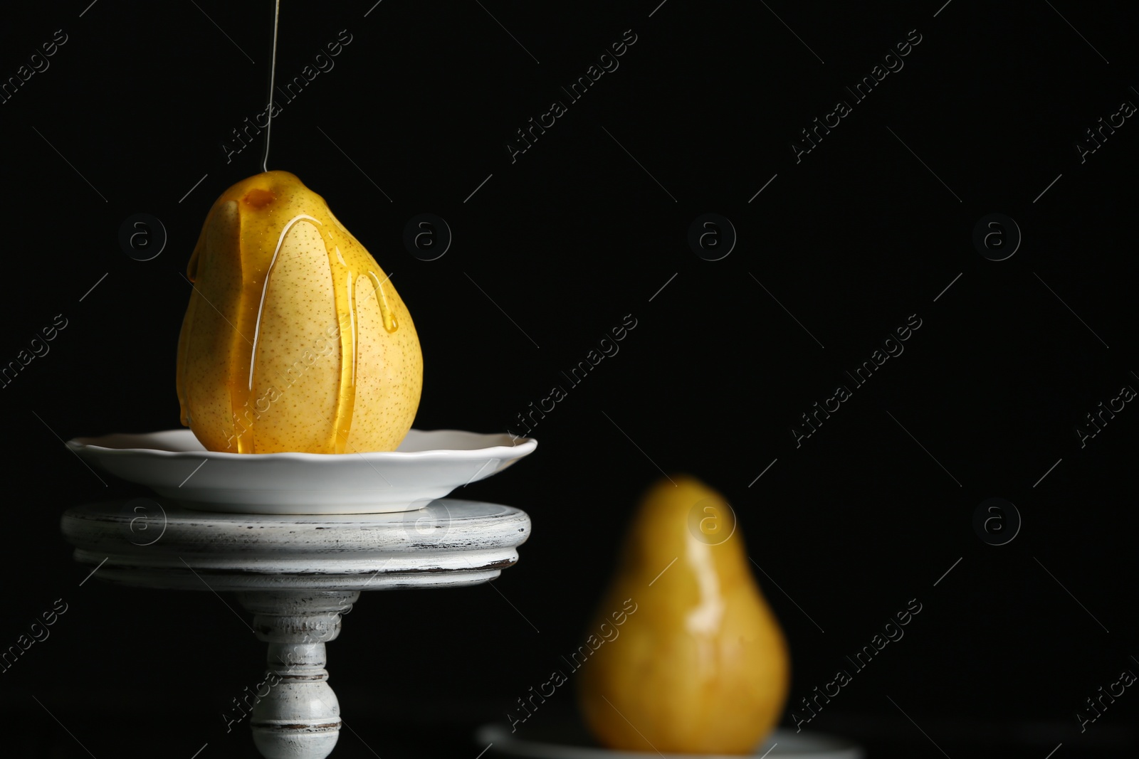 Photo of Pouring sweet syrup onto fresh ripe pear on stand against dark background. Space for text