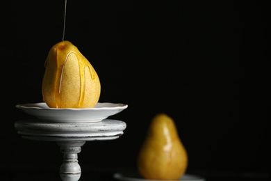 Pouring sweet syrup onto fresh ripe pear on stand against dark background. Space for text