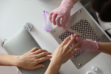 Professional manicurist filing client's nails in beauty salon, top view