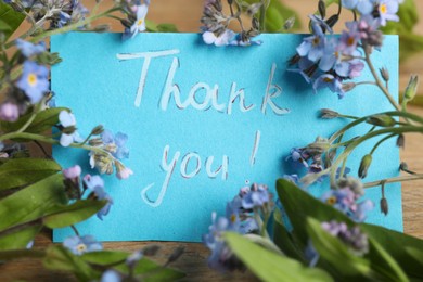 Photo of Card with phrase Thank You and beautiful forget-me-not flowers on table, closeup