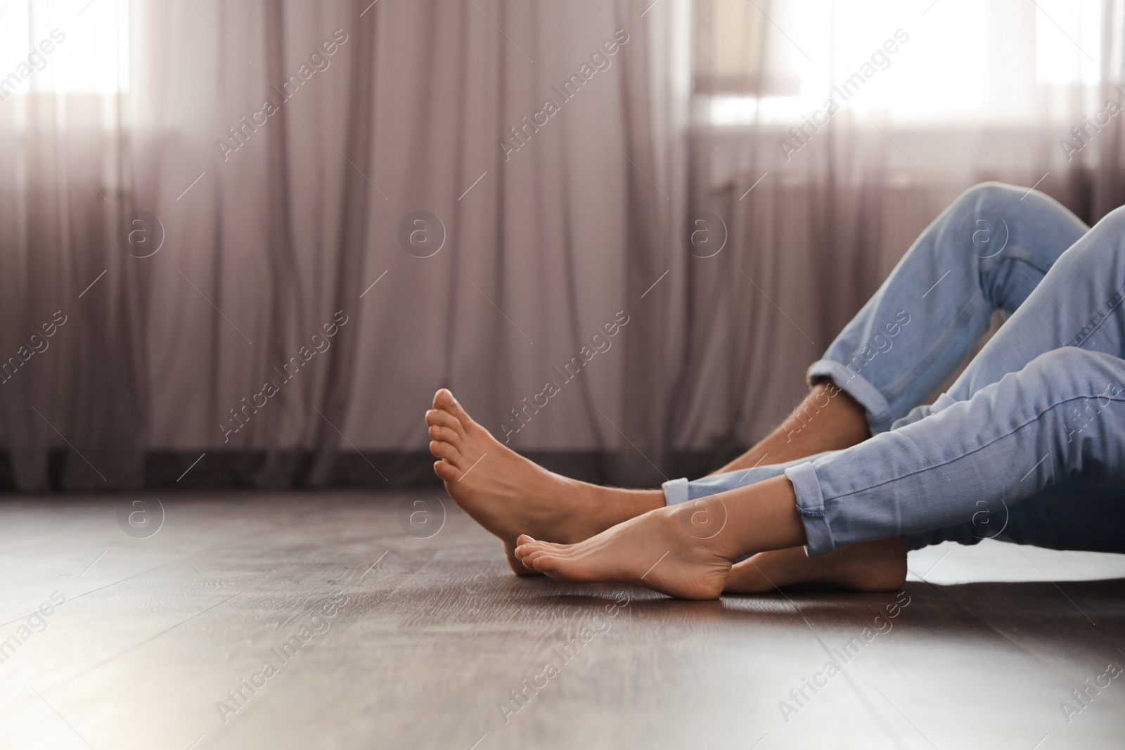 Photo of Barefoot couple sitting on warm floor at home, closeup view with space for text. Heating system
