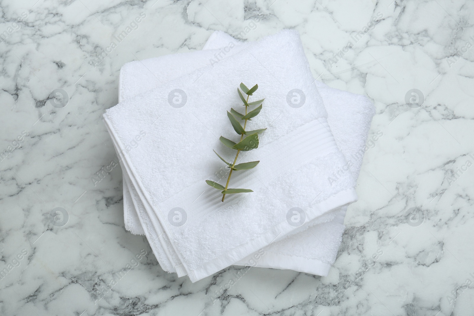 Photo of Folded terry towels and eucalyptus branch on white marble table, top view