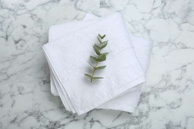 Folded terry towels and eucalyptus branch on white marble table, top view