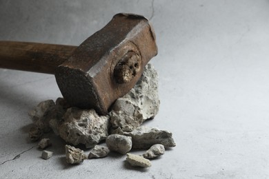 Photo of One sledgehammer and pieces of broken stones on grey background, closeup. Space for text