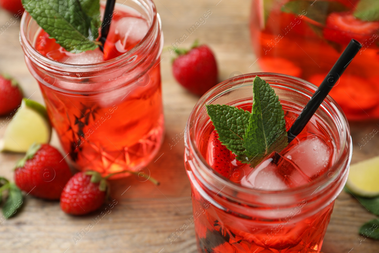Photo of Refreshing drink with strawberry and lime on wooden table, closeup