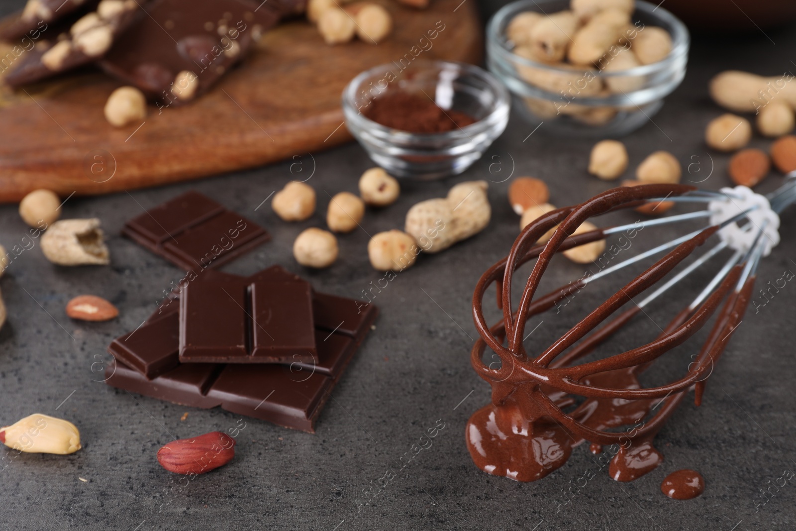 Photo of Whisk with chocolate cream and ingredients on gray table, closeup