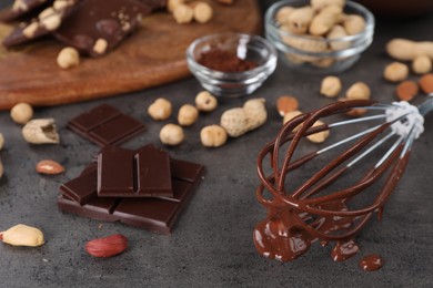 Whisk with chocolate cream and ingredients on gray table, closeup