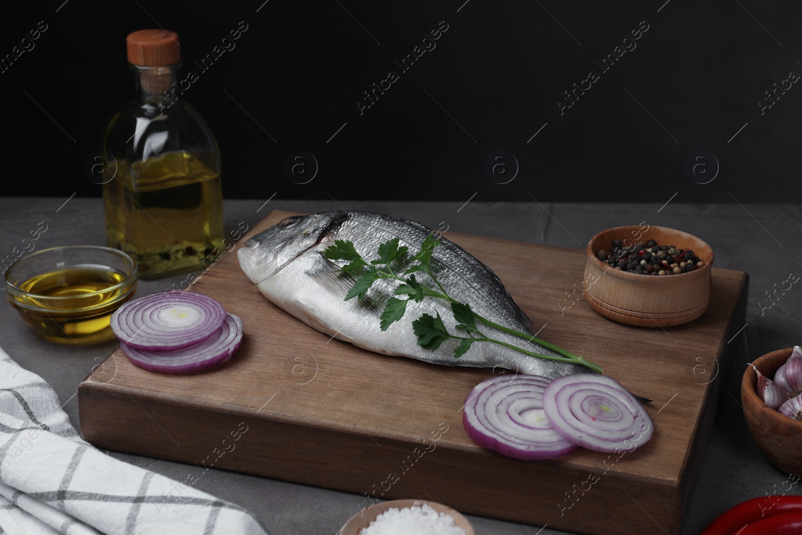 Photo of Raw dorado fish, spices, onion and oil on grey table