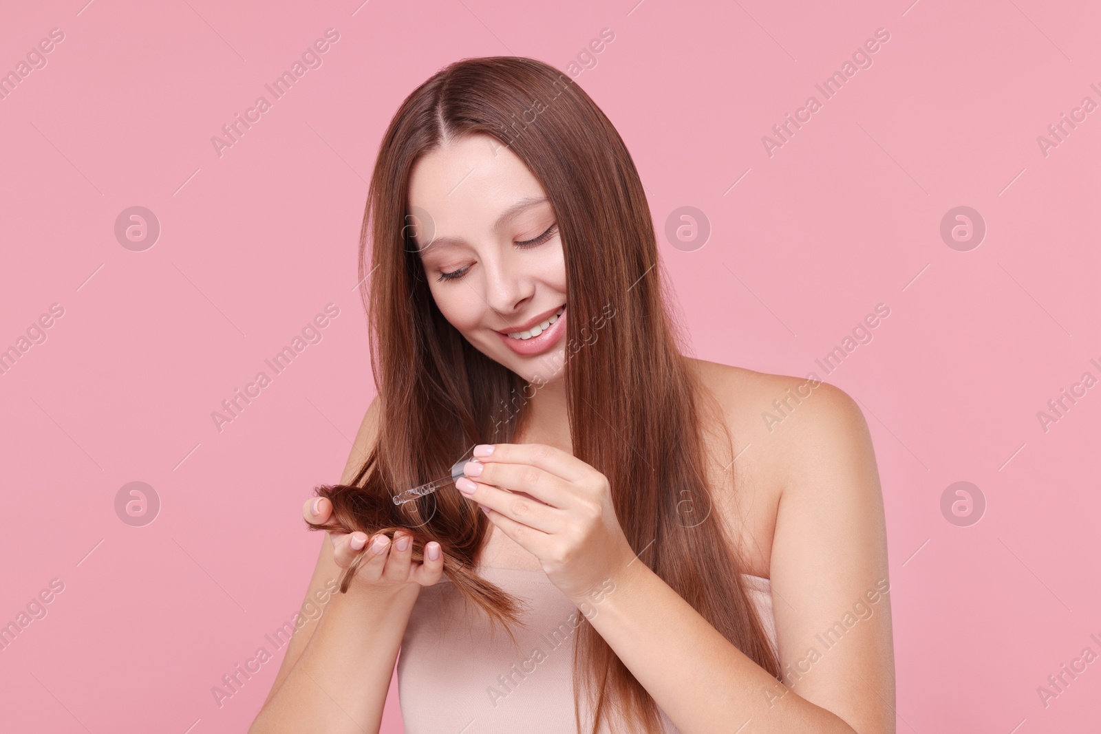 Photo of Beautiful woman applying serum onto hair on pink background