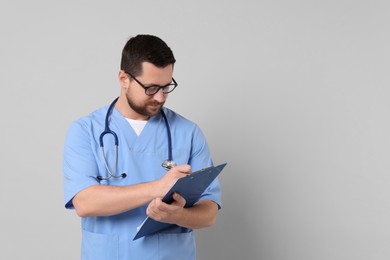 Photo of Doctor with clipboard and stethoscope on light grey background. Space for text