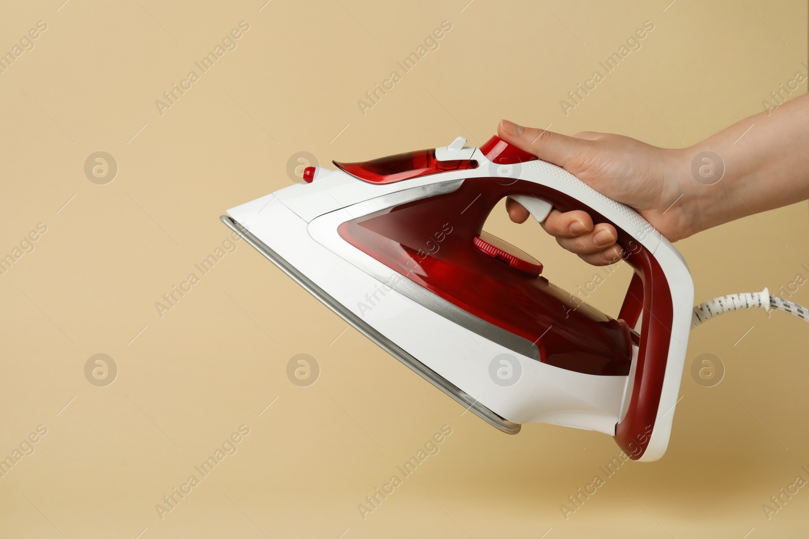 Photo of Woman holding modern iron on beige background, closeup